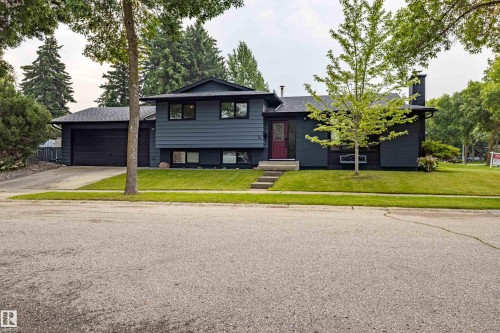 Modern Contemporary home featuring a striking black exterior with clean architectural lines, attached two-car garage, and a professionally landscaped front yard with mature trees and manicured lawn - 14 Brunswick Crescent, St. Albert, AB 
