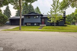 Modern Contemporary home featuring a striking black exterior with clean architectural lines, attached two-car garage, and a professionally landscaped front yard with mature trees and manicured lawn - 
