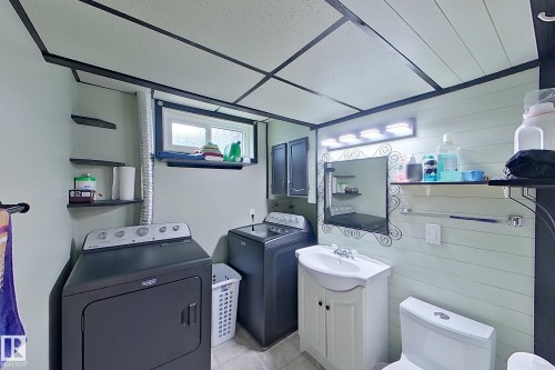 Dedicated laundry room featuring full-size front-load washer and dryer, white cabinetry with ample storage, utility sink with chrome fixtures, and recessed lighting throughout - 14 Brunswick Crescent, St. Albert, AB 