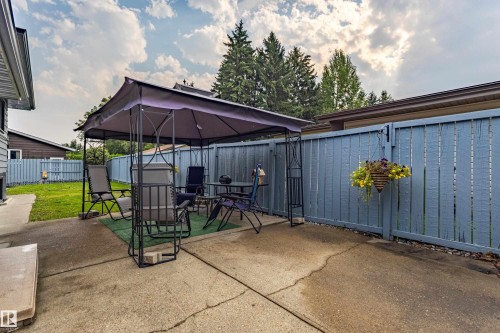 Outdoor entertaining space featuring a retractable canopy shade structure, concrete patio foundation, and mature landscaping with evergreen trees - 14 Brunswick Crescent, St. Albert, AB 
