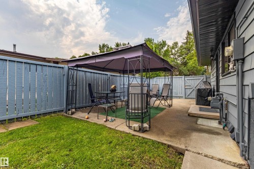 Spacious backyard oasis featuring a covered patio structure with integrated seating area, manicured lawn, mature landscaping, concrete hardscape, and direct access to the home's exterior - 14 Brunswick Crescent, St. Albert, AB 