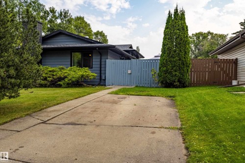 Welcoming single-story residence with a spacious concrete driveway, mature landscaping including tall evergreen specimens, and lush lawn areas flanking the home - 14 Brunswick Crescent, St. Albert, AB 