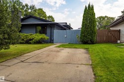 Welcoming single-story residence with a spacious concrete driveway, mature landscaping including tall evergreen specimens, and lush lawn areas flanking the home - 