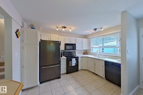 Bright, updated kitchen featuring stainless steel appliances, white cabinetry, tile flooring, ample counter space, and abundant natural light from large windows - 14 Brunswick Crescent, St. Albert, AB 
