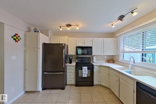 Kitchen featuring white cabinetry, light-toned countertops, a stainless steel refrigerator, black range, and an undermount sink - 14 Brunswick Crescent, St. Albert, AB 