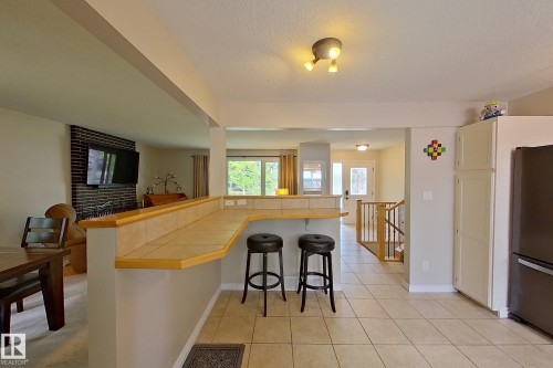 Open-concept kitchen and dining area featuring a wood-finish island with seating for two, tile flooring, stainless steel refrigerator, recessed ceiling lighting, and expansive windows providing natural light throughout the space - 14 Brunswick Crescent, St. Albert, AB 