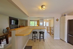 Open-concept kitchen and dining area featuring a wood-finish island with seating for two, tile flooring, stainless steel refrigerator, recessed ceiling lighting, and expansive windows providing natural light throughout the space - 