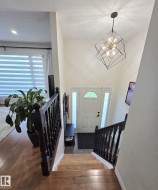 Two-story entryway featuring a modern geometric chandelier, wood-finish flooring, and a white entry door with frosted sidelights - 