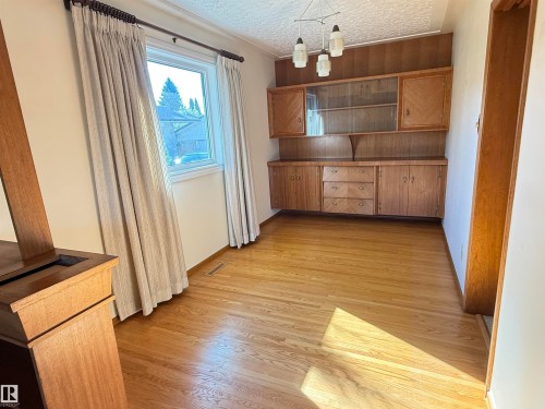 Bright, naturally lit dining room featuring warm wood-finish flooring, built-in cabinetry with glass-front upper shelving and storage drawers, pendant lighting, and large window with soft drapery allowing abundant natural light - 7007 91 Avenue Nw, Edmonton, AB 