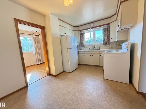 Spacious kitchen featuring stainless steel appliances, including refrigerator, range, and dishwasher, paired with white cabinetry and a ceramic tile countertop - 7007 91 Avenue Nw, Edmonton, AB 