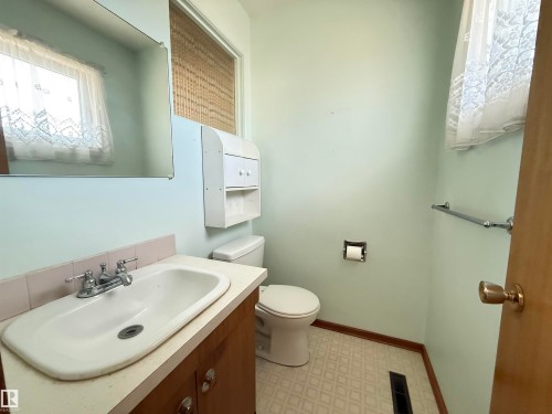 Bathroom featuring a pedestal sink with chrome faucet, porcelain toilet, tile flooring, and ample natural light from multiple windows - 7007 91 Avenue Nw, Edmonton, AB 
