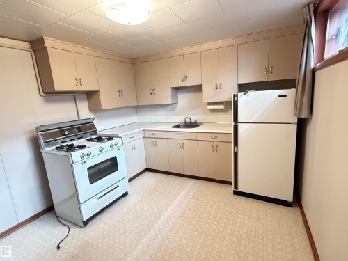 Efficient kitchen layout featuring white cabinetry with chrome hardware, gas range with white enamel finish, stainless steel refrigerator, and ceramic tile flooring - 7007 91 Avenue Nw, Edmonton, AB 