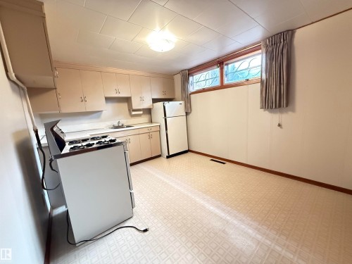 Spacious basement kitchen featuring classic cabinetry, gas range, refrigerator, and dishwasher - 7007 91 Avenue Nw, Edmonton, AB 