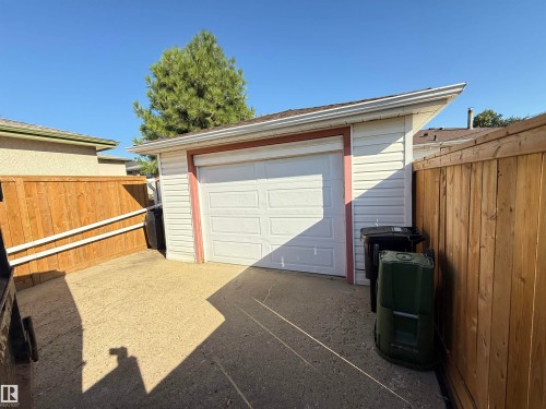 Detached garage with white paneled overhead door and concrete driveway apron, framed by wooden privacy fencing on both sides - 7007 91 Avenue Nw, Edmonton, AB 