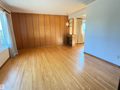 Spacious living area showcasing warm wood-finish flooring, rich wood-paneled accent wall with built-in cabinetry, and abundant natural light from multiple windows - 7007 91 Avenue Nw, Edmonton, AB 
