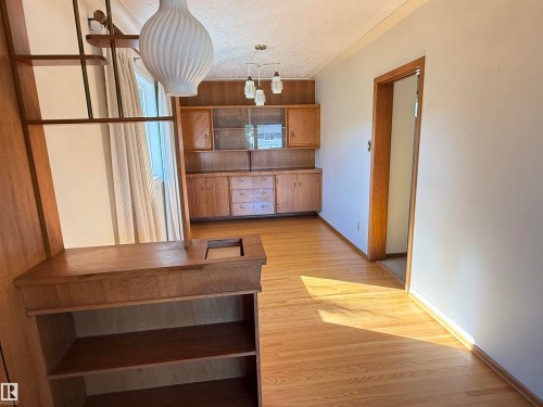 Bright open living area featuring warm wood-finish flooring, built-in cabinetry with glass-front display doors, and pendant lighting - 7007 91 Avenue Nw, Edmonton, AB 