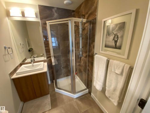 Walk-in corner shower with glass enclosure, single vanity with wood-finish cabinetry, rectangular vessel sink, and large wall-mounted mirror - #308 9907 91 Av Nw, Edmonton, AB 