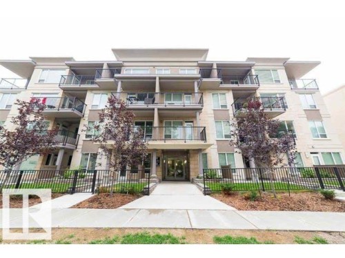 Multi-story building featuring light-colored exterior, multiple balconies with dark railings, and a central entrance - #308 9907 91 Av Nw, Edmonton, AB 