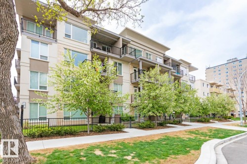 Contemporary multi-story building featuring light-toned exterior with stone accents, individual balconies with black railings, and a row of flowering trees along the sidewalk - #308 9907 91 Av Nw, Edmonton, AB 