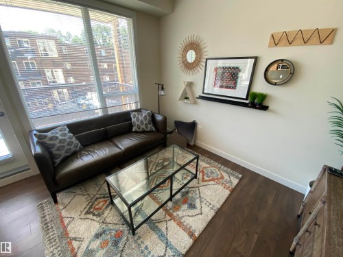 Expansive window with blinds, dark wood-finish flooring, light wall color, and a dark leather sofa - #308 9907 91 Av Nw, Edmonton, AB 