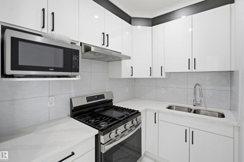 White cabinetry with matte black hardware, stainless steel gas range, over-the-range microwave, dual basin undermount sink, and light-toned countertops - 2027 13 Avenue Nw, Edmonton, AB 