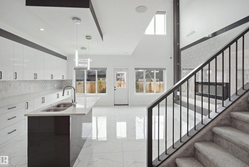 Contemporary kitchen with white cabinetry, a large island featuring an undermount double sink, and sleek tile flooring - 2027 13 Avenue Nw, Edmonton, AB 