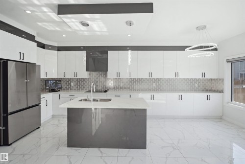 Modern kitchen featuring white cabinetry, a central island with a sink, stainless steel appliances, and tile flooring - 2027 13 Avenue Nw, Edmonton, AB 