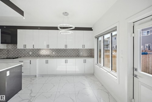 Sleek kitchen featuring white gloss cabinetry, a patterned tile backsplash, recessed lighting, and a contemporary chandelier - 2027 13 Avenue Nw, Edmonton, AB 