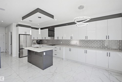 Modern kitchen featuring a central island with a sink, extensive white cabinetry, a tiled backsplash, and stainless steel appliances - 2027 13 Avenue Nw, Edmonton, AB 