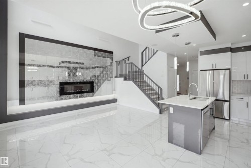 Porcelain tile flooring, recessed electric fireplace, white cabinetry with stainless steel appliances, central kitchen island with undermount sink, and a modern chandelier - 2027 13 Avenue Nw, Edmonton, AB 