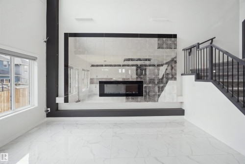 Spacious interior featuring high ceilings, large windows, a built-in fireplace with a decorative tiled surround, and a staircase with metal railings - 2027 13 Avenue Nw, Edmonton, AB 
