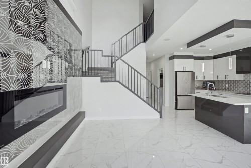 Two-story ceiling, contemporary staircase with metal railings, built-in electric fireplace with decorative accent wall, white tile flooring, and kitchen island with an undermount sink - 2027 13 Avenue Nw, Edmonton, AB 
