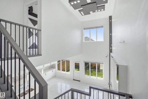 Vaulted ceiling with a contemporary lighting fixture, staircase with metal balusters, white tile flooring, and white cabinetry - 2027 13 Avenue Nw, Edmonton, AB 