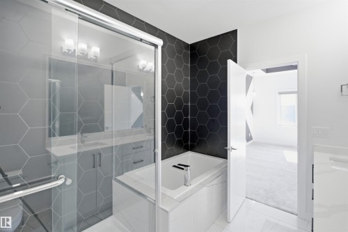 Hexagonal wall tiling, white soaking tub, frameless glass shower enclosure, dual vanity with undermount sinks, and white countertop - 2027 13 Avenue Nw, Edmonton, AB 