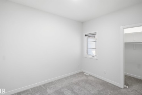 Recessed window with roller shade, neutral wall paint, light gray carpeting, and a closet with built-in shelving - 2027 13 Avenue Nw, Edmonton, AB 