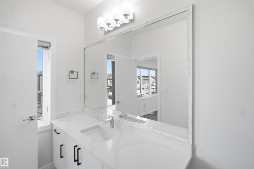 White vanity with black cabinet pulls, integrated rectangular sink, polished chrome faucet, and expansive wall mirror with a decorative frame - 2027 13 Avenue Nw, Edmonton, AB 