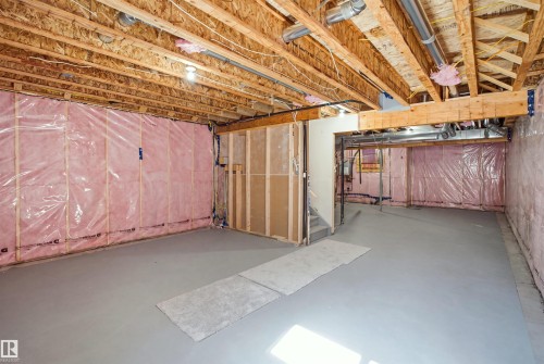 Unfinished basement featuring exposed wood joists, insulated walls, concrete flooring, and a partial wood-framed wall - 2027 13 Avenue Nw, Edmonton, AB 