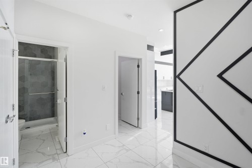 White tile flooring, geometric wall accent, white walls, and a shower with hexagonal tile and glass enclosure - 2027 13 Avenue Nw, Edmonton, AB 