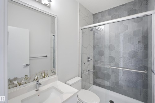 Modern bathroom featuring a glass-enclosed shower, hexagon pattern wall tile, a white vanity with an integrated sink, and a chrome faucet - 2027 13 Avenue Nw, Edmonton, AB 
