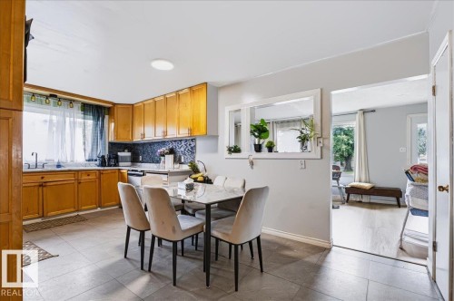 Kitchen with wood-finish cabinetry, patterned tile backsplash, and light-toned tile flooring - 12919 135 Avenue Nw, Edmonton, AB 