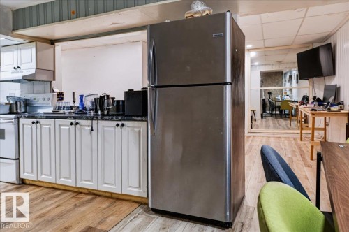 Kitchen area with white cabinetry, a stainless steel refrigerator, and wood-finish flooring - 12919 135 Avenue Nw, Edmonton, AB 