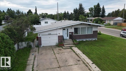 Ranch-style residence featuring a white facade with horizontal brown siding accents, an attached single-car garage, and a concrete driveway - 12919 135 Avenue Nw, Edmonton, AB 
