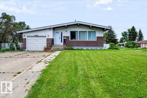 Single-story exterior with a white garage door, white entry door, and a concrete driveway - 12919 135 Avenue Nw, Edmonton, AB 