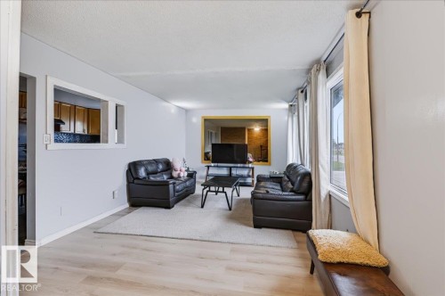 Spacious living area featuring light-toned wood-finish flooring, white walls, and a large window with white trim - 12919 135 Avenue Nw, Edmonton, AB 