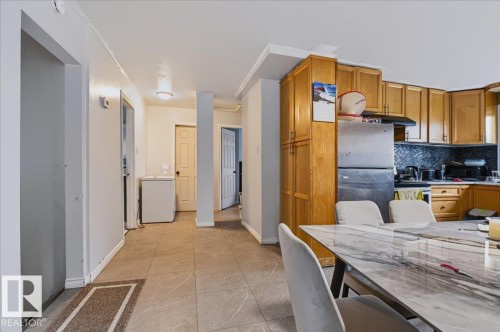 Kitchen featuring wood cabinetry, stainless steel refrigerator, tile backsplash, and tile flooring - 12919 135 Avenue Nw, Edmonton, AB 