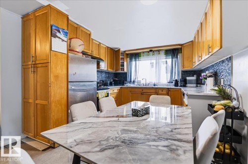 Full wood-finish cabinetry, stainless steel appliances, mosaic tile backsplash, and a large window above the sink - 12919 135 Avenue Nw, Edmonton, AB 