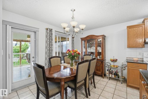 Tiled flooring throughout, chandelier lighting, wood-finish cabinetry, white tile backsplash, and an exterior glass door - 3231 28A Avenue Nw, Edmonton, AB 