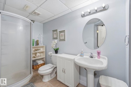 Curved glass shower enclosure, pedestal sink, wall-mounted oval mirror, three-light vanity fixture, and white cabinetry - 3231 28A Avenue Nw, Edmonton, AB 
