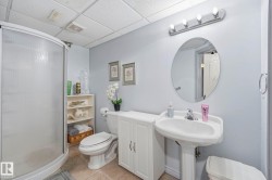 Curved glass shower enclosure, pedestal sink, wall-mounted oval mirror, three-light vanity fixture, and white cabinetry - 