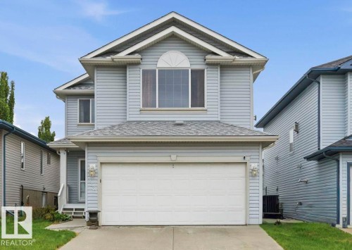 Two-story residence featuring light gray siding, a prominent arched window, a two-car garage, and an inviting front entrance with porch lighting - 3231 28A Avenue Nw, Edmonton, AB 